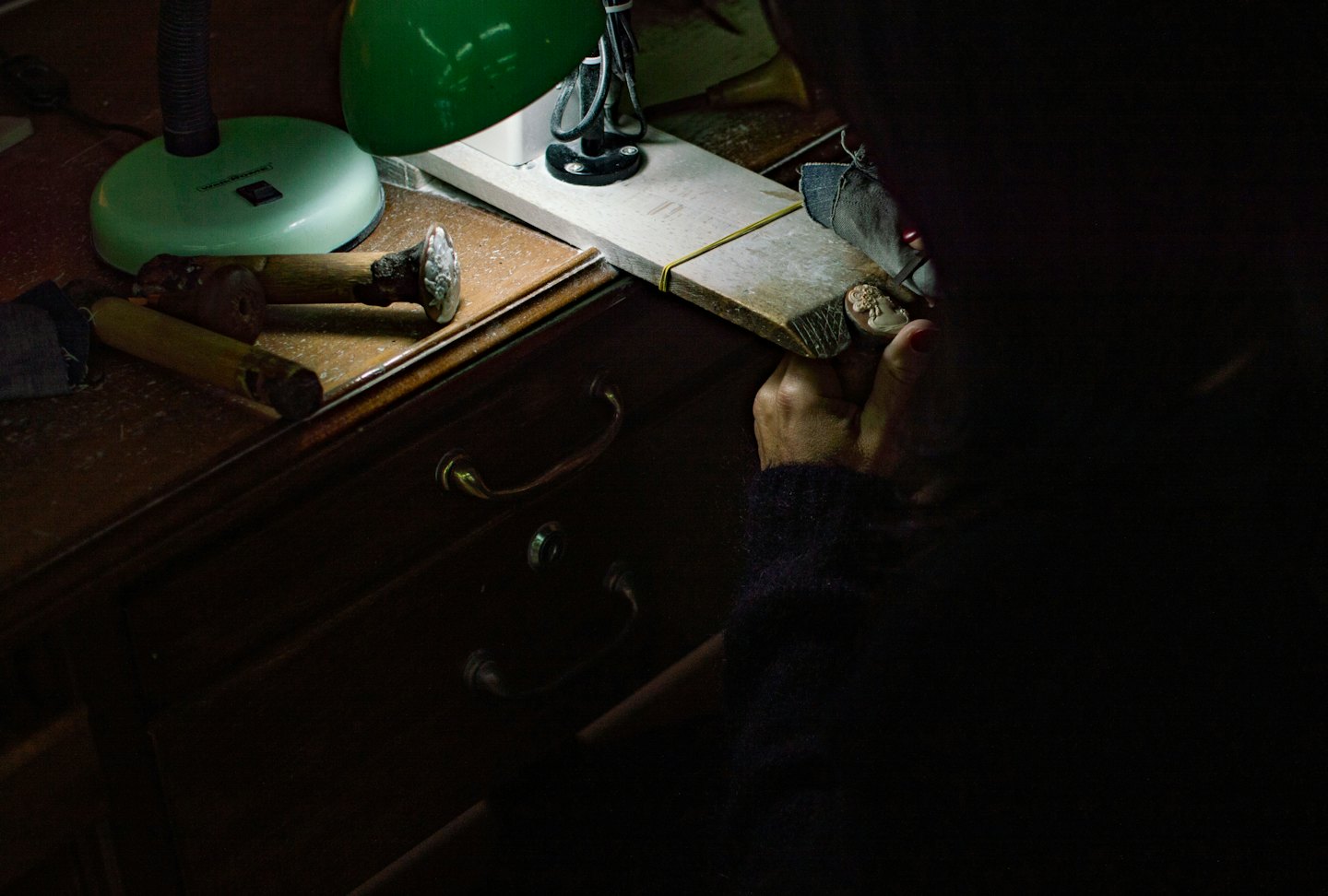Craftsperson carves an intricate object at a wooden workbench.
